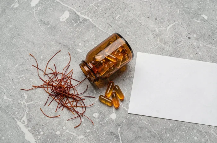 Vue de dessus de capsules de safran dorées et de filaments de safran sur une surface en pierre, illustrant un complément alimentaire naturel